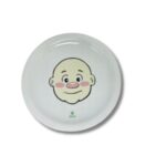 Prato de cerâmica branco, quadrado, com um desenho de um rosto de menino sorrindo, decorado com brócolis como cabelo e outros alimentos para formar um rosto divertido.