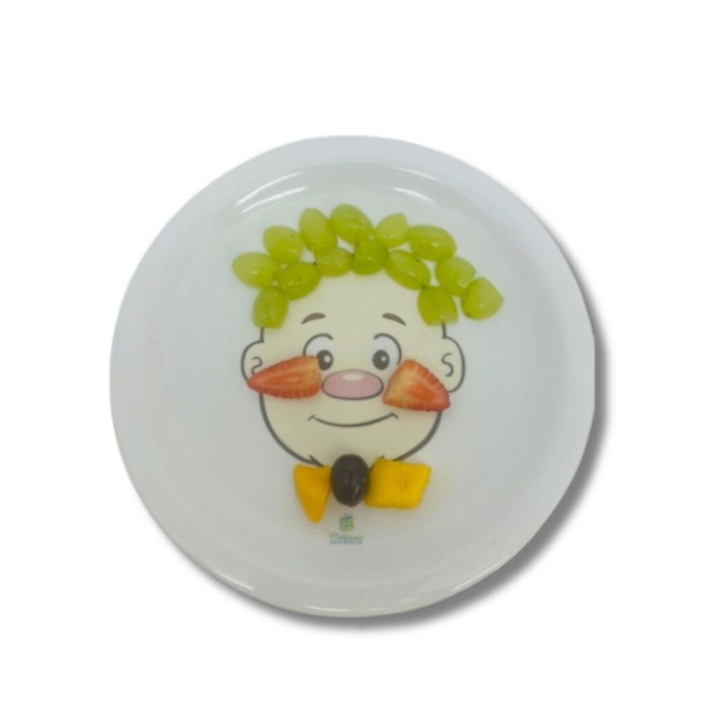 Prato de cerâmica branco, quadrado, com um desenho de um rosto de menino sorrindo, decorado com brócolis como cabelo e outros alimentos para formar um rosto divertido.