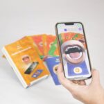Baralho dos Sons em Realidade Aumentada da Materiais para Brincar, mostrando uma das cartas com a ilustração de uma boca e um celular ao lado, exibindo o efeito de realidade aumentada.