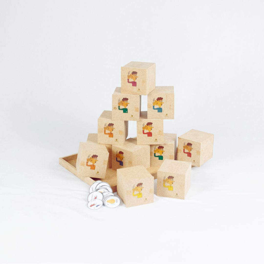 Brincar de escutar 2 Kit Brincar de Escutar da Materiais para Brincar, mostrando uma bandeja com 12 caixinhas de madeira, com uma criança usando uma das caixinhas para ouvir o som.