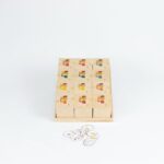 Kit Brincar de Escutar da Materiais para Brincar, mostrando uma bandeja com 12 caixinhas de madeira, com uma criança usando uma das caixinhas para ouvir o som.