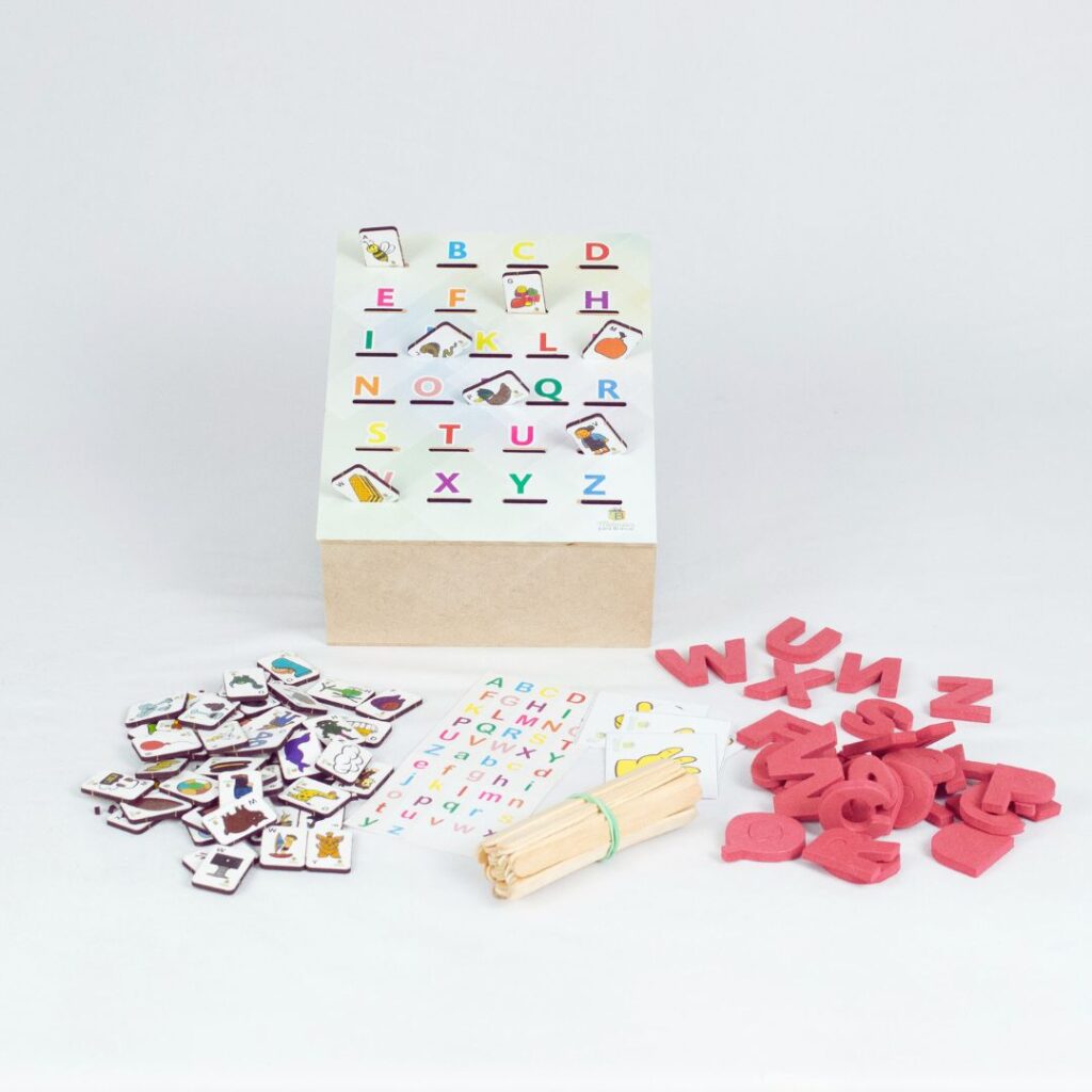Kit Caixa Alfabeto da Materiais para Brincar, mostrando uma caixa de MDF aberta com diversos materiais de alfabetização, incluindo fichas com figuras, alfabetos em EVA e palitos.
