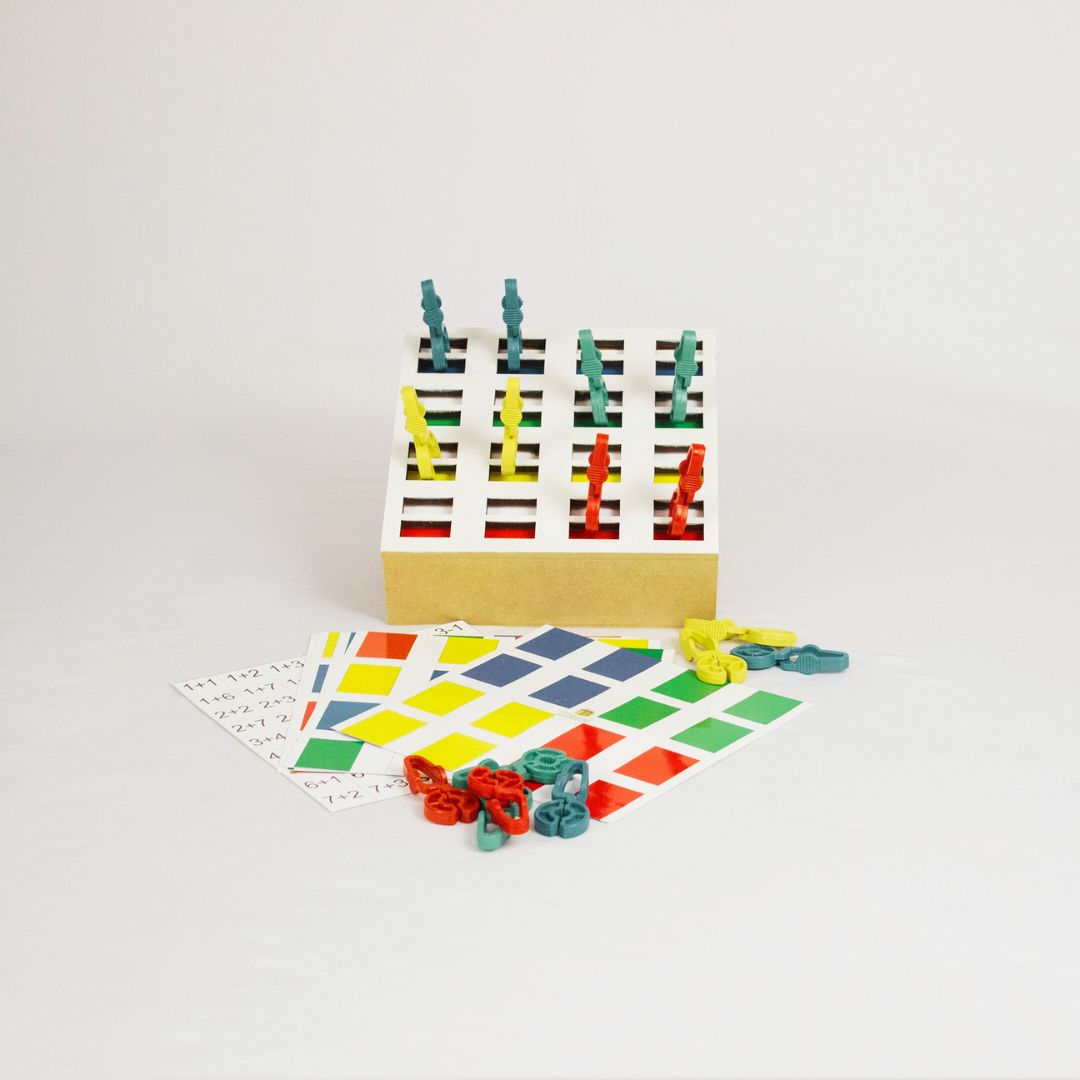 Caixa de pregadores bola Kit Caixa de Pregadores Bola da Materiais Para Brincar, mostrando uma caixa em MDF com pregadores coloridos e uma cartela de sequências. Uma mão está usando um dos pregadores.