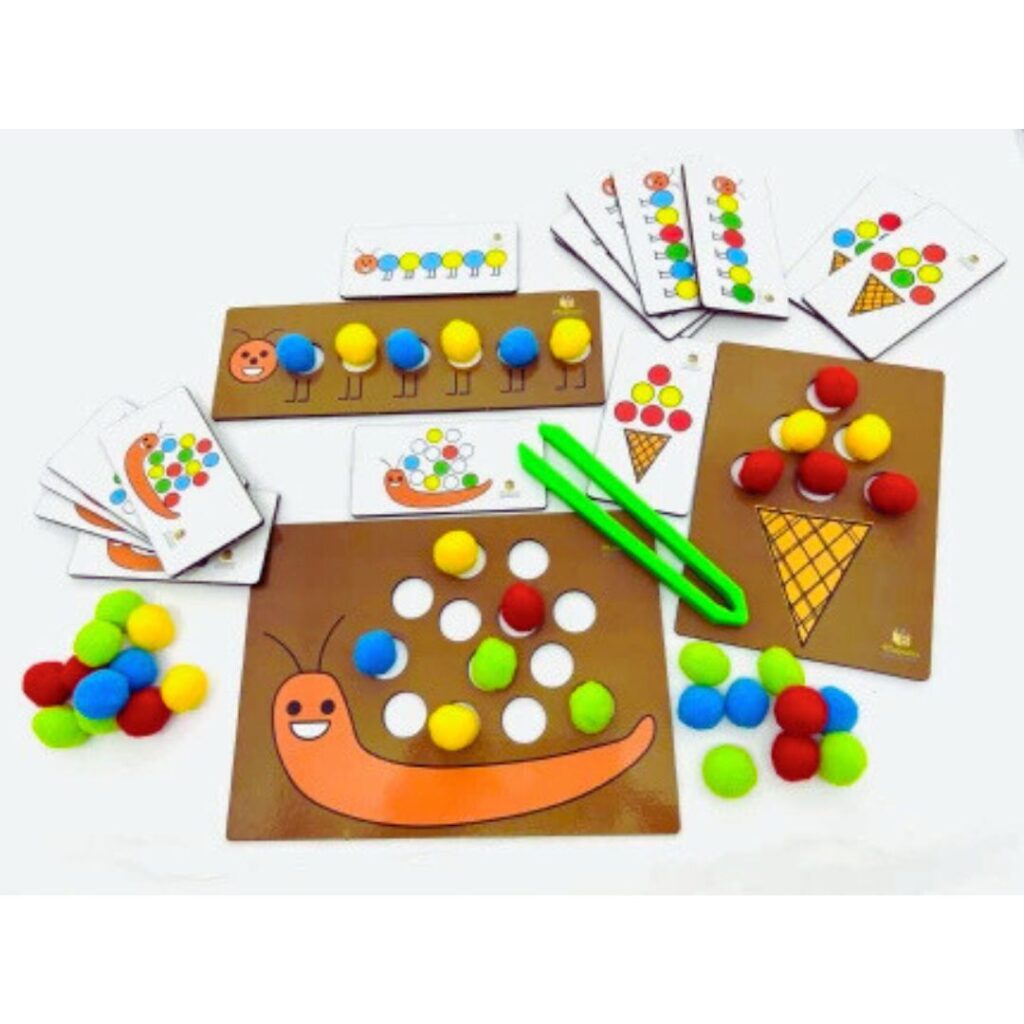 Jogo Centopeia, Caracol e Sorvete da Materiais Para Brincar, mostrando uma das placas de MDF com alguns pompons coloridos já inseridos nos furos, e uma criança usando a pinça para colocar outro pompom.