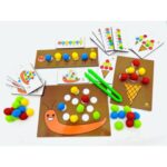 Jogo Centopeia, Caracol e Sorvete da Materiais Para Brincar, mostrando uma das placas de MDF com alguns pompons coloridos já inseridos nos furos, e uma criança usando a pinça para colocar outro pompom.