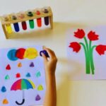 Laboratório das Cores da Materiais Para Brincar, mostrando um suporte de madeira com tubos de ensaio preenchidos com líquidos coloridos. Os frascos dos corantes primários e um conta-gotas gigante estão ao lado.