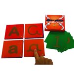 Kit Letras e Números Texturizados da Materiais Para Brincar. Uma mão de criança está usando o dedo para traçar a superfície texturizada de uma das cartas, que mostra a letra 'A' em relevo.