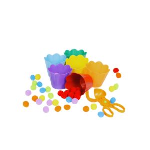 Kit Tesoura, Pompons e Potes Coloridos da Materiais Para Brincar, mostrando uma tesoura de transferência sendo usada por uma mão de criança para pegar um pompom azul de uma tigela e colocá-lo em um pote da mesma cor.